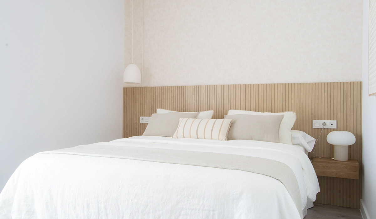 "Dormitorio minimalista con cabecero de listones de madera, ropa de cama en tonos neutros y lámparas de diseño moderno