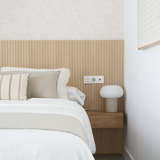 Detalle de dormitorio con cabecero de listones de madera, mesilla flotante y lámpara de diseño moderno en tonos neutros